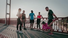 Young sports persons rest standing on footbridge. Multiracial athletic people talk and warm up relaxing leg muscles after running workout in summer morning - Powered by Shutterstock - Get 15% off with code: PIKWIZARD15