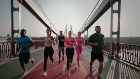 Group of young athletes of different races runs together on running track on bridge over river. Sportive males and females train under blue sky at sunrise - Powered by Shutterstock - Get 15% off with code: PIKWIZARD15