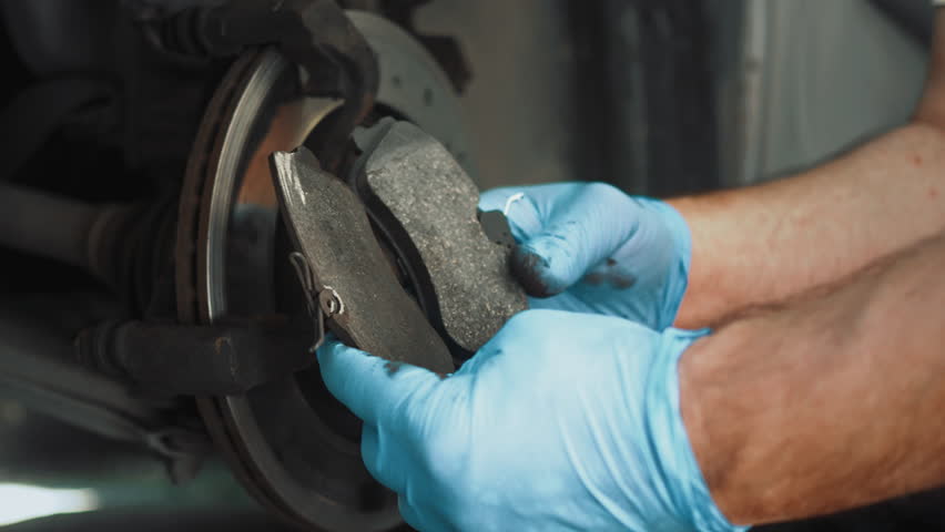 vehicle maintenance. Auto mechanic working on car brakes in mechanics garage. Close-up male hands compares old and new pads before installation. Wear gloves Royalty-Free Stock Footage #1105674477
