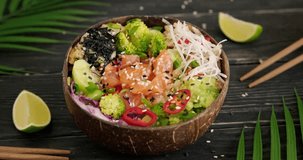 Eating salmon poke using chopsticks, tasting Hawaiian dish with raw fish cubes, cucumber and nori. Poke served in natural coconut bowl. Close up slow motion video, 4k horizontal footage
