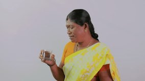 This video is about A south indian woman drinking water in glass on plain background
