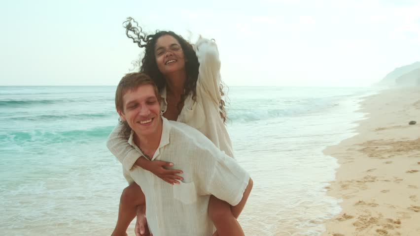 Young happy multi ethnic couple of Indian woman and Caucasian man have good time at seaside resort and record video about trip to sunny island walk along sandy wild beach. Lifestyle, vacation, ocean
