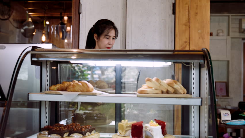 Shop owner is checking bakery, open candy cabinet bend down check bakery in cabinet, in order receive orders online that people have ordered, before confirming order be ready be delivered customer. Royalty-Free Stock Footage #1105691173