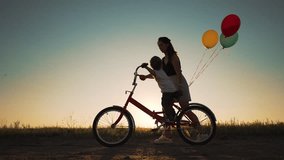 Happy family. Mom teaches son to ride bike. Concept of children holiday and dreams. Family playing in park at sunset. Silhouette of mom and son on a bike in the park. Green energy. Mom teaches son. - Powered by Shutterstock - Get 15% off with code: PIKWIZARD15