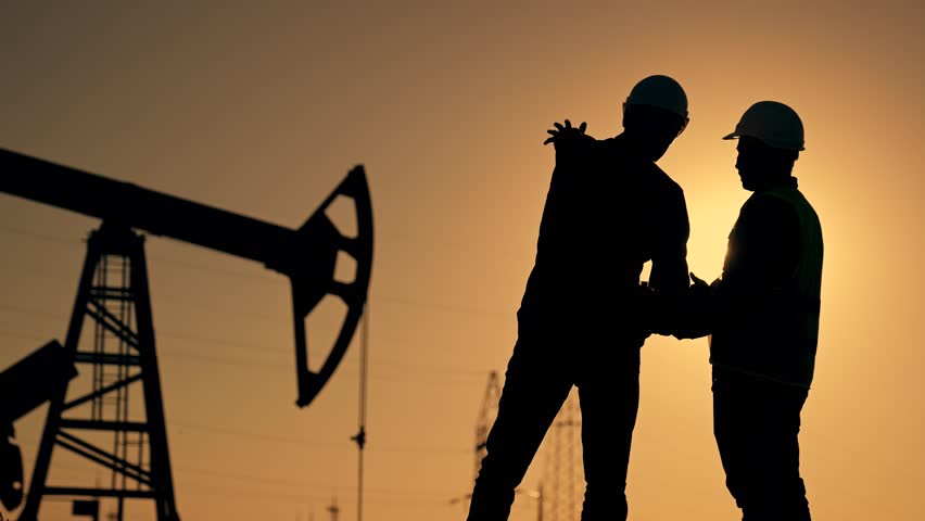 Teamwork. Two workers in hard hats at sunset. Working oil pump silhouette. Two engineers work on an oil pump at sunset. Extraction of crude oil minerals. Field of oil resources production of gasoline