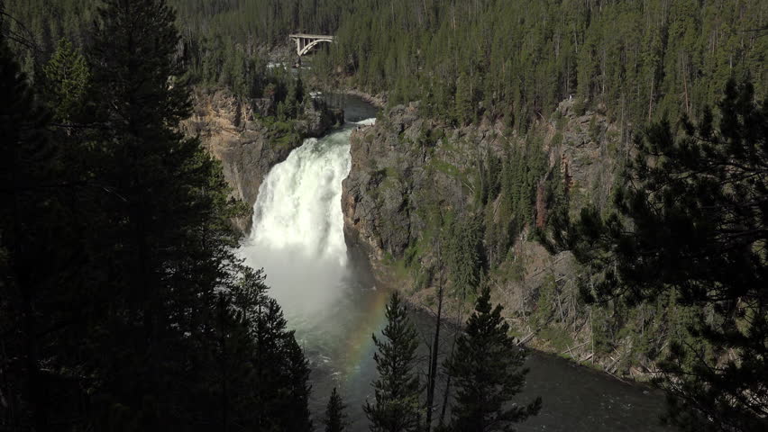 YELLOWSTONE, WYOMING - JUN 2015: Upper Falls Yellowstone River through forest rainbow 4K. The upper falls 109 feet high. Beautiful powerful environmental geology. Park created by Ulysses S. Grant 1872