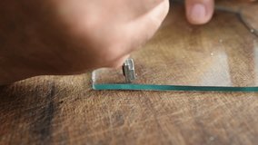 The video shows how the hands of the glazier with a glass cutter draw a line along the glass, thereby cutting off a piece from the glass.