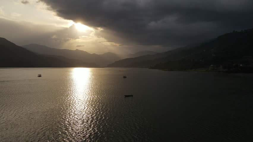 Smooth drone flight over Phewa Lake with a floating paddle boat overlooking the Nepal Valley in Pokhara during sunset. 4k footage.