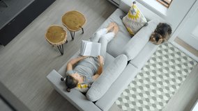 Overhead view of woman reading the book, lying on couch at home - Powered by Shutterstock - Get 15% off with code: PIKWIZARD15