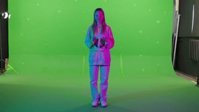 Horizontal shot on green screen background. VR or AR at home. Beautiful girl puts on a virtual reality helmet. Pink turquoise light. Cute woman in augmented reality clicks invisible buttons.