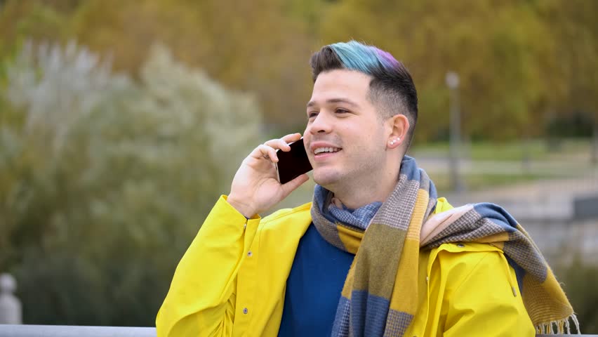 Young man wearing a yellow raincoat talking on smart phone in the street in autumn.