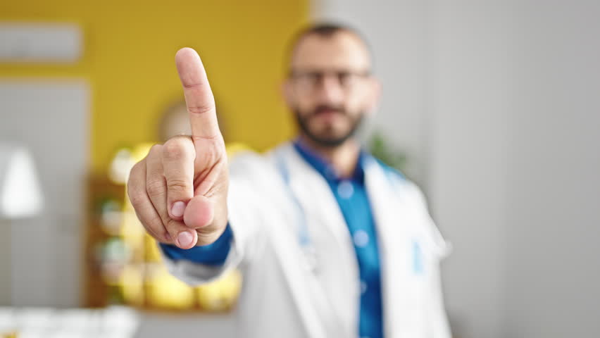 Young hispanic man doctor standing with serious expression saying no with finger at clinic Royalty-Free Stock Footage #1105717267