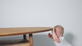 A 6 month old baby learns to stand on his feet leaning on a table. studio video on light background