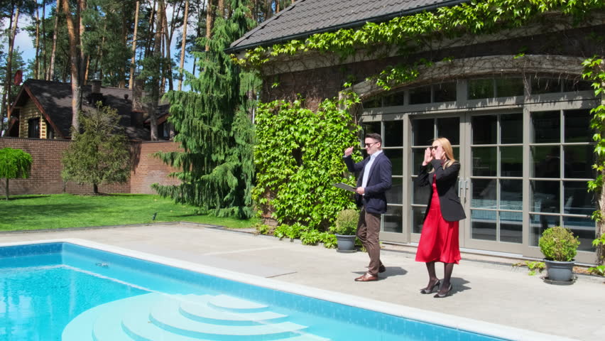 Blonde businesswoman inspects summer house offered by real estate management company. Client listens to realtor description of swimming pool