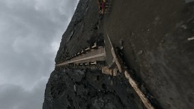 Vertical video. Aerial view flying over volcano tourist stairs crater fog mist gas fumes travel adventure extreme. FPV sport drone shot touristic people going up staircase volcanic geology formation