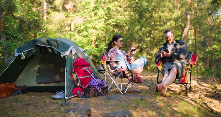 A middle aged couple relaxing during a camping break. They sit in smartphones and share funny pictures and stories with each other. Slow motion 4k footage.