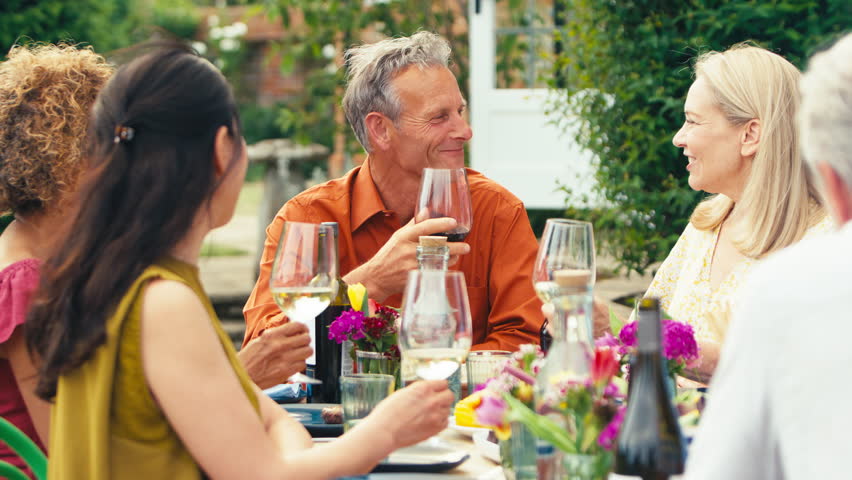Group of mature friends sitting around table talking and making a toast with wine at summer drinks party in garden at home - shot in slow motion Royalty-Free Stock Footage #1105729629