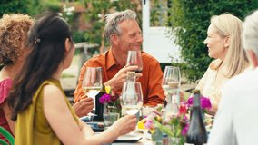 Group of mature friends sitting around table talking and making a toast with wine at summer drinks party in garden at home - shot in slow motion - Powered by Shutterstock - Get 15% off with code: PIKWIZARD15