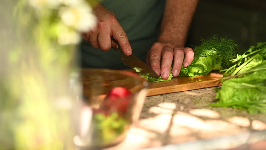 Anonymous man slicing salad and herbs in rustic kitchen
