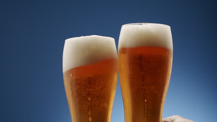 Two glasses full of frothy beer they collide in the middle on a blue background, Close up. the foam rises nicely in different parts, Macro shooting. Beautiful drops on the glass