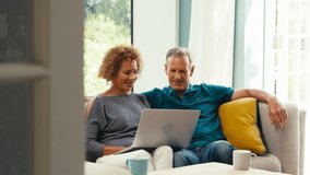 Smiling senior retired couple sitting on sofa at home making video call on laptop and waving to family- shot in slow motion - Powered by Shutterstock - Get 15% off with code: PIKWIZARD15