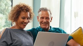 Smiling senior retired couple sitting on sofa at home making video call on laptop and waving to family- shot in slow motion - Powered by Shutterstock - Get 15% off with code: PIKWIZARD15