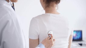Doctor and patient are at the usual medical inspection in the clinic. Therapist examines a young woman's back with a stethoscope. Medicine concept