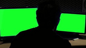 Silhouette of an Anonymous Man Working at Studio with Two Computer Monitors with Green Screen. Close Up.
