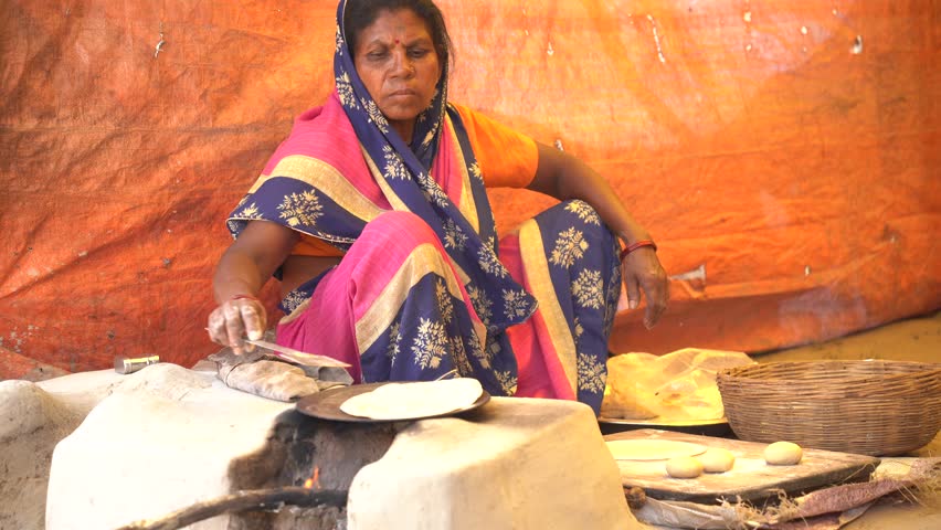 NAGPUR, MAHARASHTRA, INDIA 25 JANUARY 2023 : Woman making and cooking baking fresh food at rural village street food restaurant in vintage kitchen using firewood in earthen Wood stove