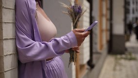 Young woman using an app on a smart phone in close up video clip. Unrecognizable female person standing in the city street with a bouquet of flowers and browsing a mobile phone