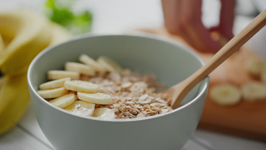 Clean eating, Caucasian woman happily adding ripe banana to a bowl of oatmeal porridge in a home kitchen. Woman preparing nutritious breakfast in slow motion, modern diet planning, homemade
 Royalty-Free Stock Footage #1105743655