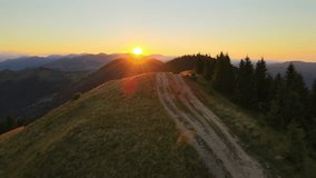 Offroad path crossing hill top. Dark dirt road illuminated with bright setting sun. Amazing sunset scenery in wild mountain forest. Beautiful nature landscape - Powered by Shutterstock - Get 15% off with code: PIKWIZARD15