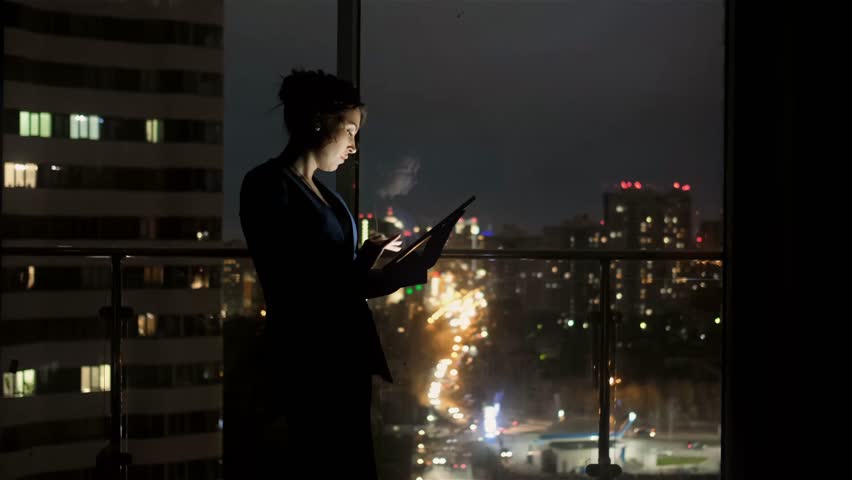 Elegant woman using gadget standing by window at home at night. Businesswoman using a tablet to work while standing by the window of an office late at night. Royalty-Free Stock Footage #1105746413