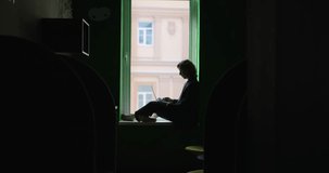 Businesswoman working concept. Silhouette of caucasian female in business suit looking at laptop during working process sitting on window sill in co-working open office space. High quality 4k video