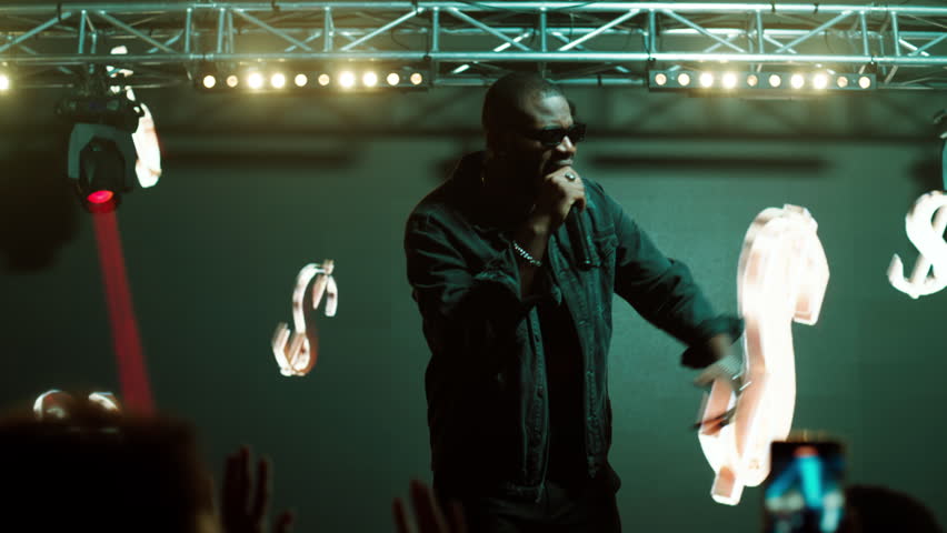 African-American rap artist performing his gig on a stage of a large venue, surrounded by bright flashig lights