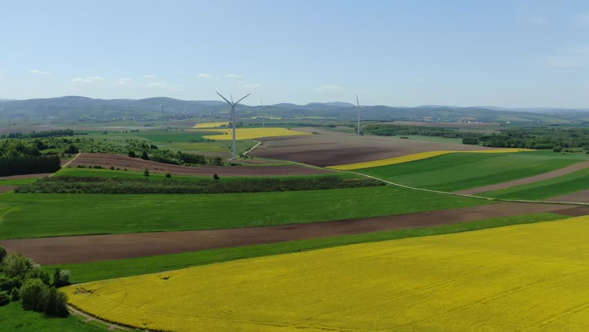 Pristine rolling green grey and yellow farm fields with windmill turbine spinning | Shutterstock HD Video #1105752129