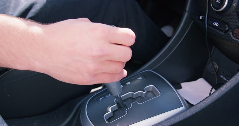 Man sits on driver seat shifting automatic transmission in car. Hand of driver moving lever arm on gearbox to add speed while driving closeup