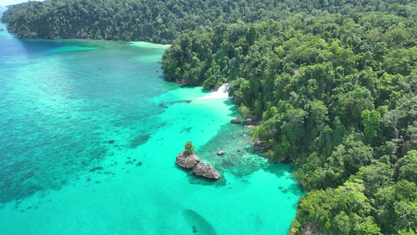 The scenic Momon waterfall tumbles from the primordial rainforest of West Papua into the shallow sea. This spectacular waterfall is found about a day
