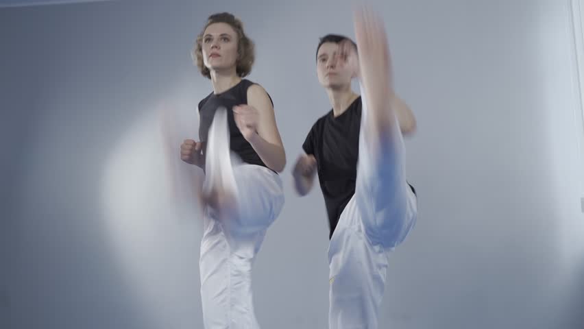 Two female athletes at taekwondo training do quick kicks. Martial arts and self defense for women. Two taekwondo fighters at training session in gym. Taekwondo practitioners training together
