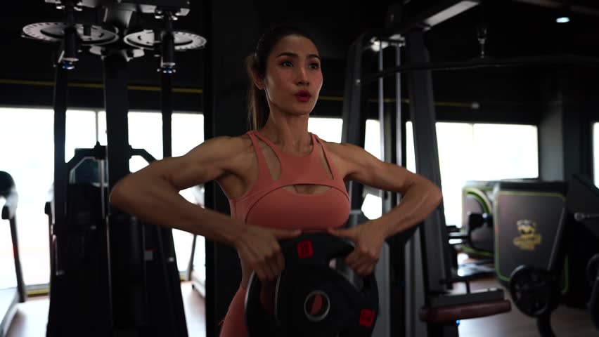 asian woman wearing sports bra doing exercise and sitting on yoga ball lifting dumbbell weights in sport gym. healthy lifestyle concept