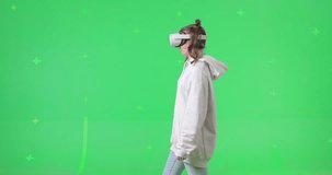 Shot on green screen background. VR or AR online at home. Cute girl in virtual reality headset. Woman turns around her axis while clicks invisible buttons and pulls virtual sliders. Internet fun.