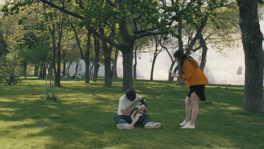 A happy couple in love sitting on the grass and playing with their cute husky.