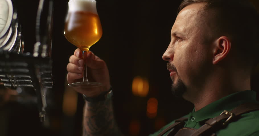 Handsome young male brewer in apron tasting fresh beer. Tasting fresh brewed beer.