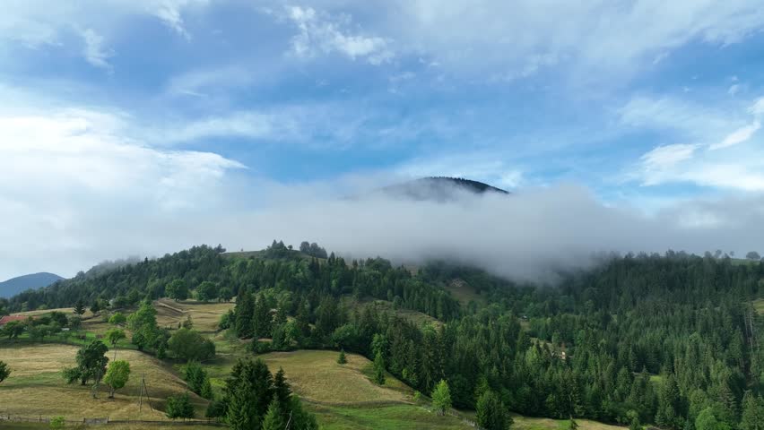 Cloudy, foggy drone landscape. Forested mountains, with roads and a village