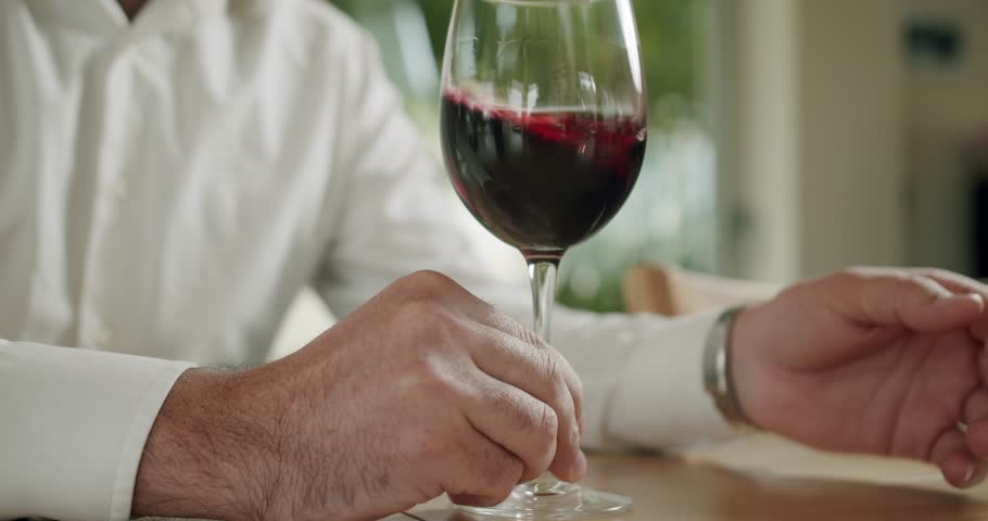 Winemaking concept. Man winemaker tasting wine. Sommelier is shaking the glass of wine and tasting it. Elegantly dressed man is tasting a flavor and drinking fresh red wine poured in transparent glass