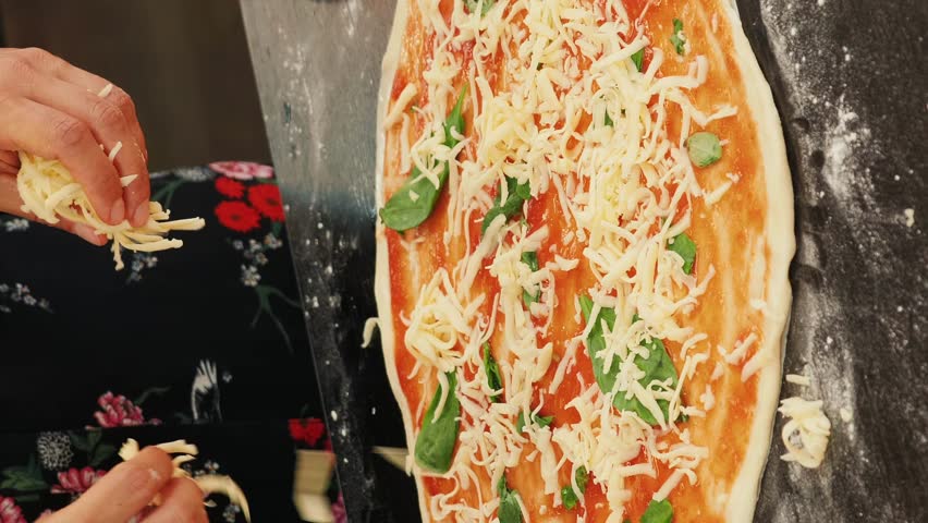Hands spreading grated cheese on pizza. Vertical video. Cooking pizza at home. Woman preparing italian homemade pizza, adding cheese on fresh dough. Process of making delicious healthy food Royalty-Free Stock Footage #1105781809