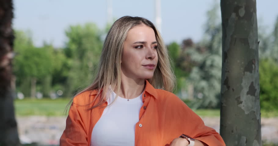 A woman sitting in a park, looking at the camera with a sad expression. The scene portrays a poignant and contemplative atmosphere, where the woman's emotions are evident through her somber gaze