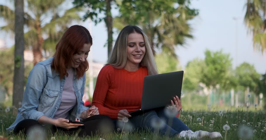 The two young women enjoying their time sitting on the beach while working on their laptops create a scene of productivity and relaxation amidst the beautiful seaside backdrop Royalty-Free Stock Footage #1105788721