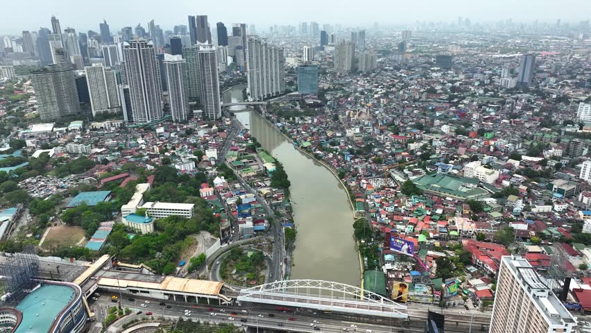 Manila cityscape at river banks aerial. Downtown area with cottages, skyscrapers, buildings. Urban Philippines city scape with streets and roads. Town drone shot. Poor Homes Along Rich Skyscrapers.
