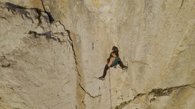 AERIAL, CLOSE UP: Climber clips in belay rope before climbing a difficult section. She is under a slightly overhanging part of a steep limestone wall. Young lady leading a route in Karst climbing area